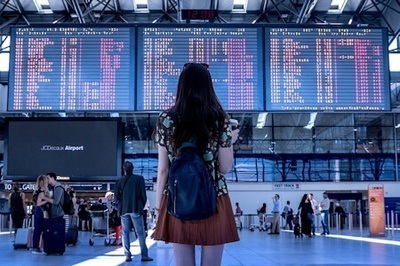 A woman wearing a skirt with her back to the camera studies the arrivals and departures board at an airport.