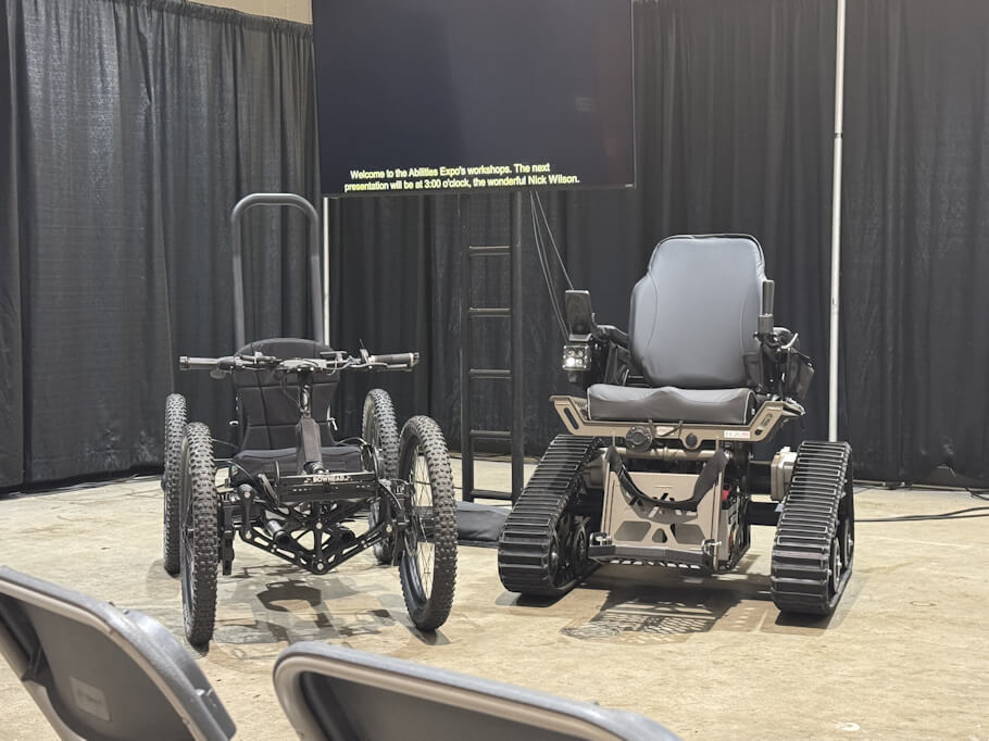 This image shows two rugged mobility devices displayed on a stage-like area inside a large indoor venue.