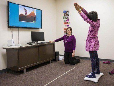 Brittany Travers, an investigator at the University of Wisconsin-Madison Waisman Center and an assistant professor of kinesiology, works with a study participant while she plays a video game designed to help youth with autism improve their balance. It may also help improve some of their autism-related symptoms - (Andy Manis).