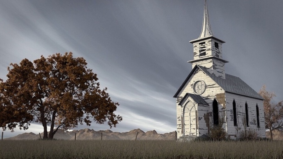 Long abandoned and neglected, a rural white church stands on unkempt grounds under gray skies beside a solitary tree and a line of old crooked fence posts. Dry, barren hills can be seen in the background.
