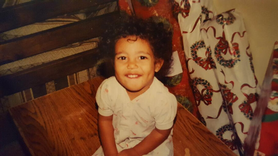 This is a warm, nostalgic photograph showing a young child with curly dark hair sitting on what appears to be a brown corduroy couch or chair.