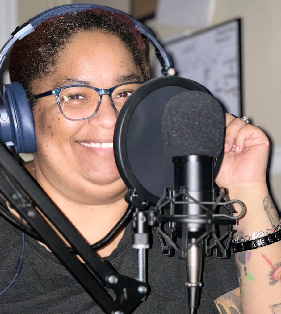 Dr. Dory Morris is seated at a professional studio microphone, wearing blue over-ear headphones and black-framed glasses.