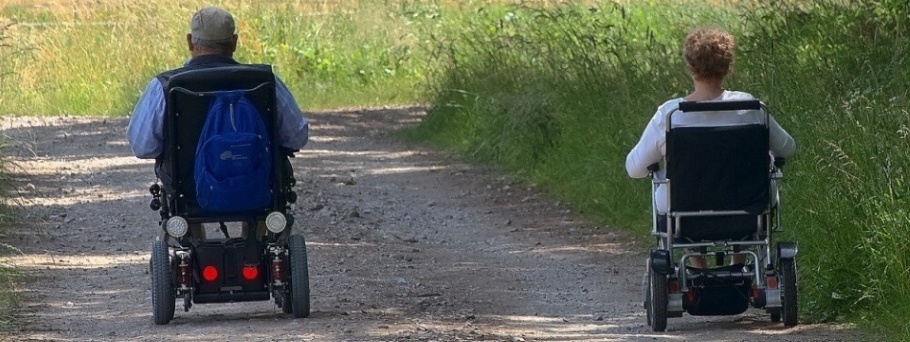Rear image of a male and female using electric wheelchairs on a country road.