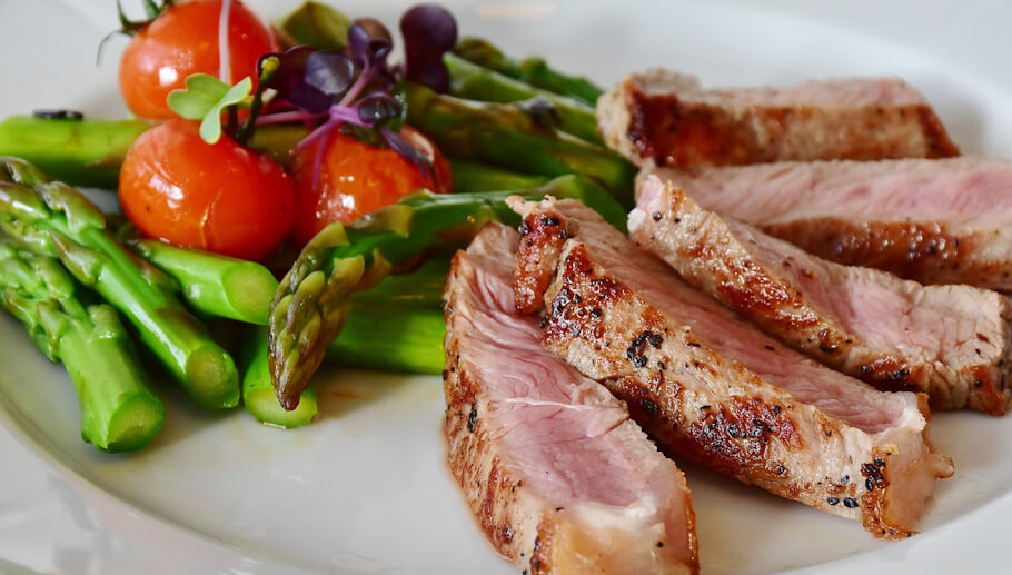 Asparagus, tomatoes, and slices of cooked meat on a plate.