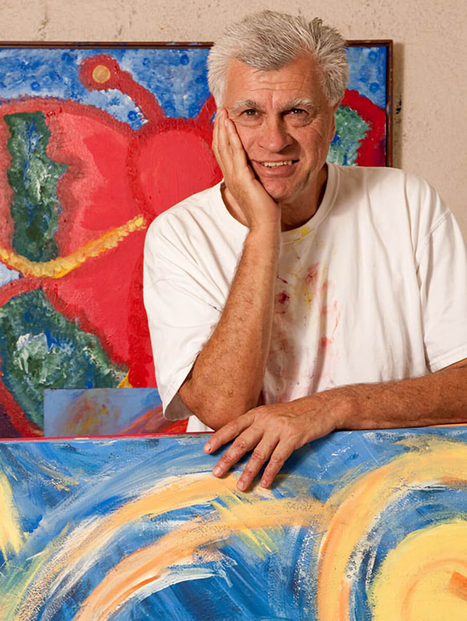 Portrait photo of George Mendoza, an older man with short white hair, smiling gently with his chin resting on his hand.
