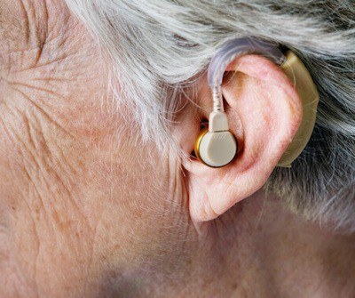 Close up photo of the left ear of a person wearing a beige colored hearing aid.