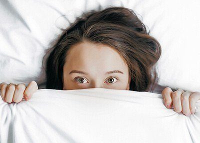 Woman under bed cover with just the top half of her face and hands showing.