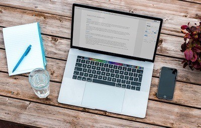 An overhead shot of a MacBook with a draft of an executive summary on a wooden surface.