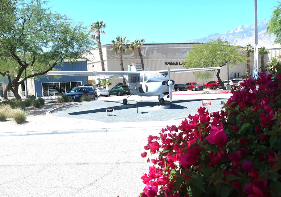The image shows a small, white propeller airplane displayed outdoors on a circular patch of gravel, surrounded by a curb.
