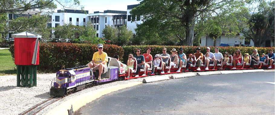 This image captures a group of people riding a miniature outdoor train on a small track.