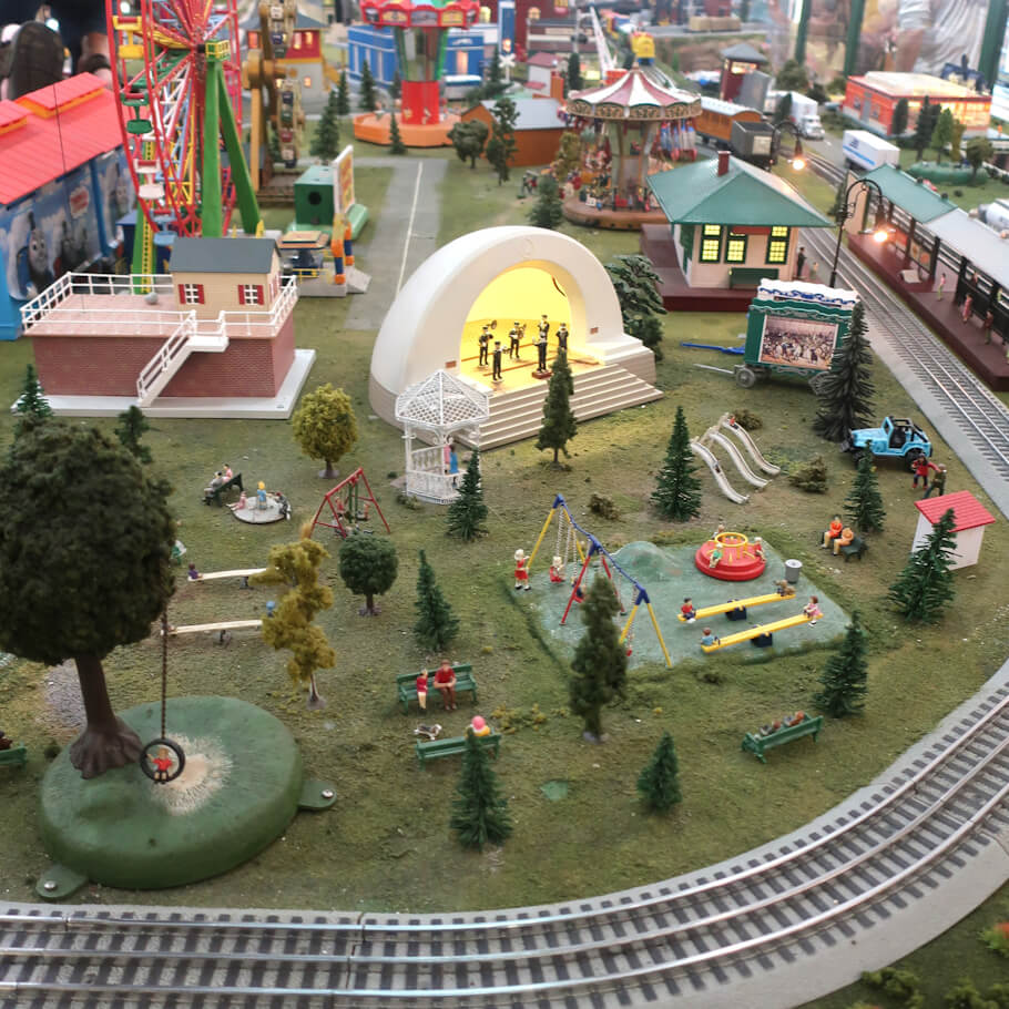 This image showcases a detailed miniature model of a lively amusement park and railway scene.