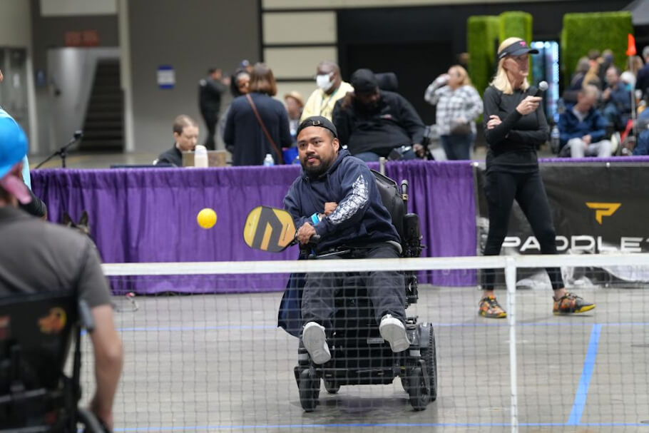 This image captures an inclusive adaptive sports moment at an indoor paddle tennis event.