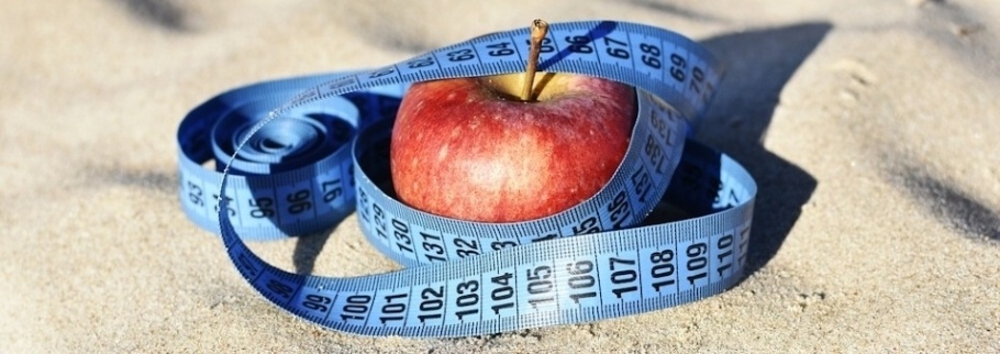 A red apple wrapped in a blue tape measure sits on a sandy surface.