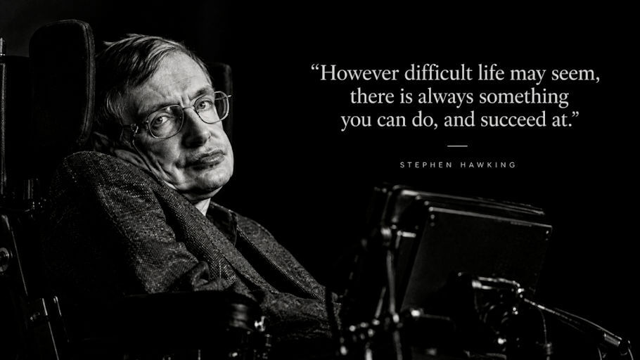 A black and white photograph of Stephen Hawking with short tousled hair and wire-rimmed glasses, seated in a high-backed motorized wheelchair against a solid black background.