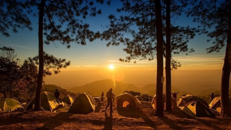 The image shows a Sunset with mountains and several camping tents and campers in the foreground.